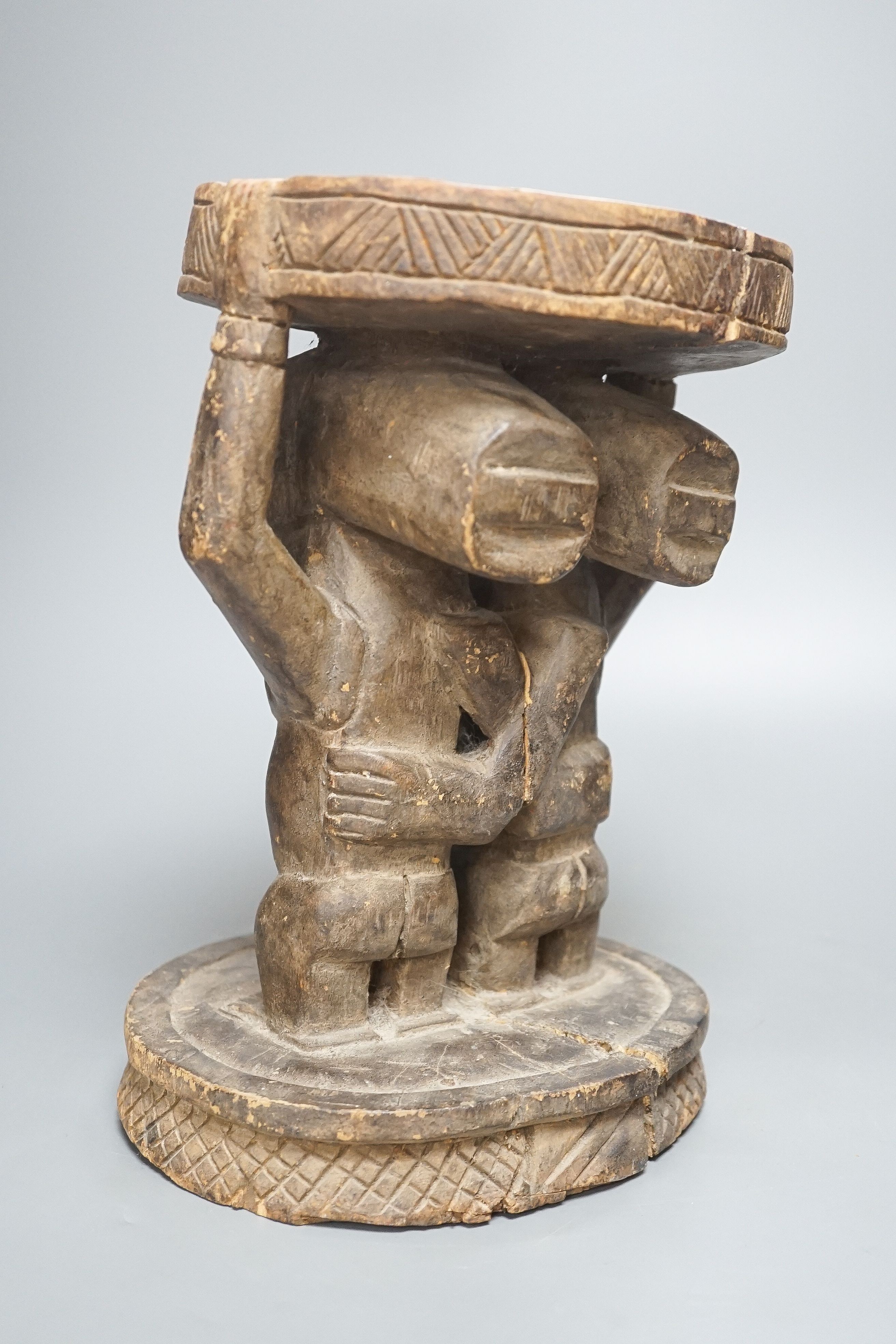 A Yoruba carved wood stool, modelled with male and female figures 27cm